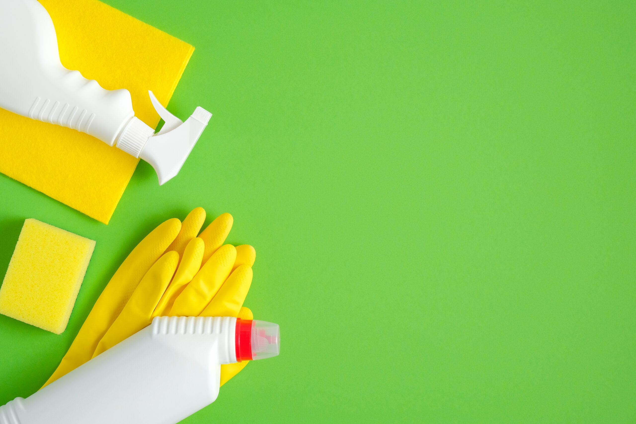 Cleaning supplies on green background. Top view cleaner spray bottle, rag, sponge, detergent, yellow rubber gloves. House cleaning service and housekeeping concept.